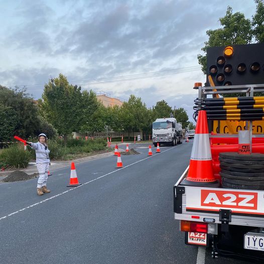 A2Z Traffic vehicle and team member directing traffic with illuminated batons on a two-way street, safely managing vehicle flow during active roadworks in a suburban Melbourne area.