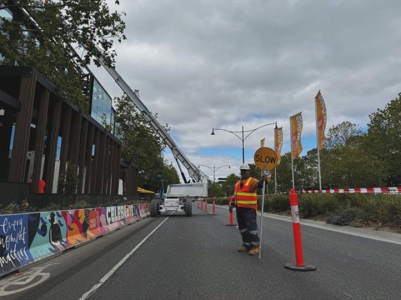 A2Z Traffic controller managing road safety at a Melbourne construction site, holding a "SLOW" sign with traffic cones and barriers in place to ensure a secure work zone.